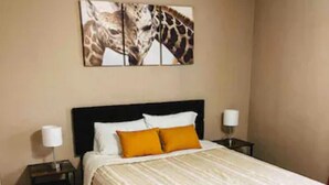 A bedroom with a large bed, two nightstands, a giraffe-themed artwork, and a tiled floor.