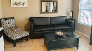 A living room with a black sofa, patterned armchair, and a coffee table with a bowl.