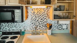 A compact kitchen with a microwave, stove, and sink. There are wooden cabinets and a tiled backsplash.