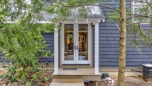 Una casa con terraza de madera, puerta de cristal y un árbol en primer plano.