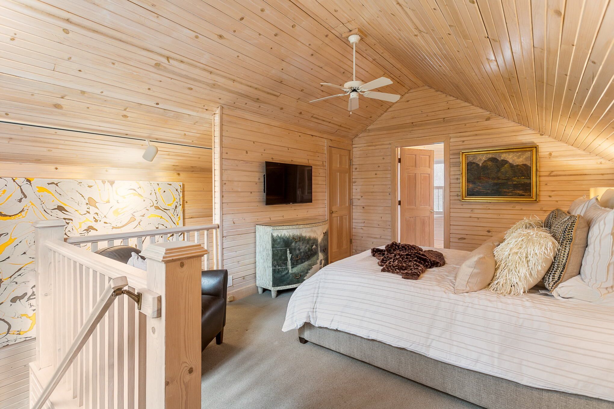 Quarto de cabana de madeira com cama, pintura, televisão e ventilador de teto.