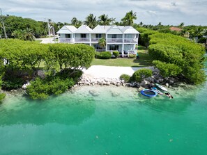 A multi-story house with a balcony, surrounded by lush greenery and a clear turquoise water body. - Beach House - Waterfront Villa - Free Kayaks (Duck Key)