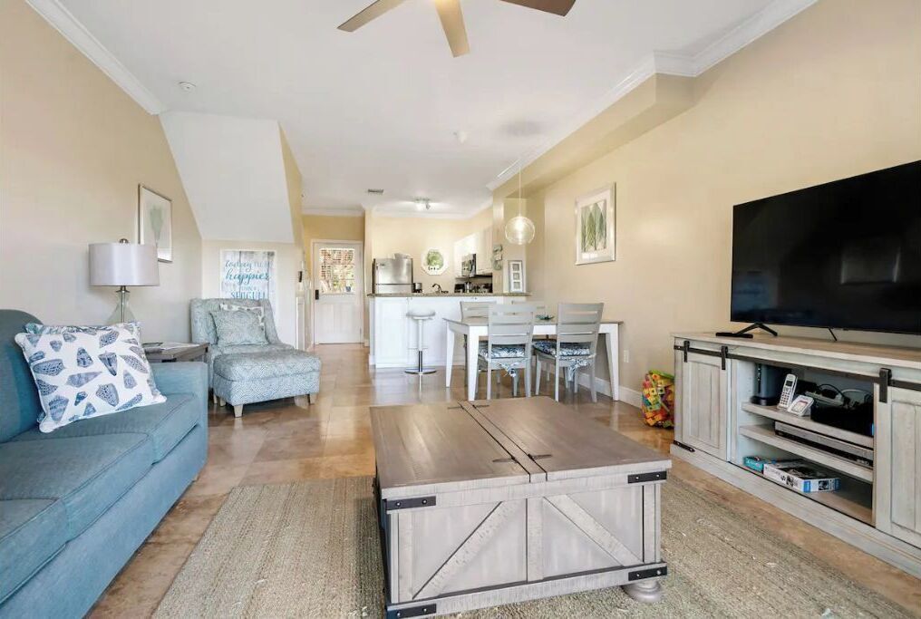 A living room with a sofa, coffee table, TV stand, and a dining area with chairs and a table.