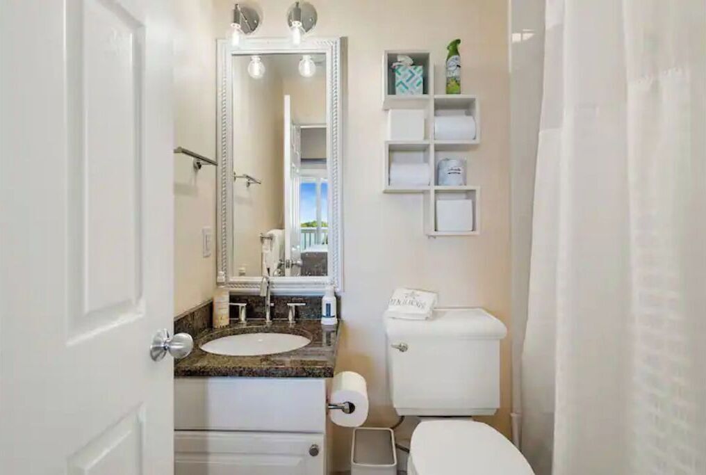 Un baño con lavamanos blanco, espejo, inodoro y cortina de ducha.