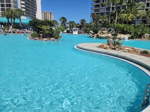 Une grande piscine extérieure à l’eau d’un bleu limpide, entourée de palmiers et bordée d’un îlot rocheux.