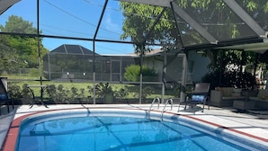 Une piscine dont le bord est revêtu de carreaux rouges et blancs, entourée d’un espace abrité comprenant des chaises et une table.