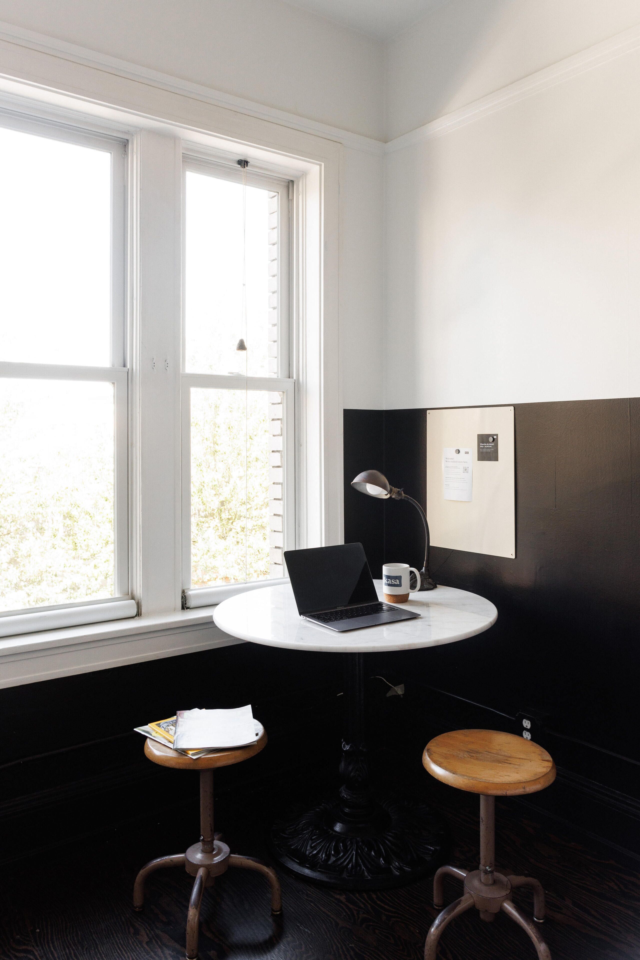 Una habitación con una mesa redonda, una computadora portátil, una taza de café y un tablón de anuncios.