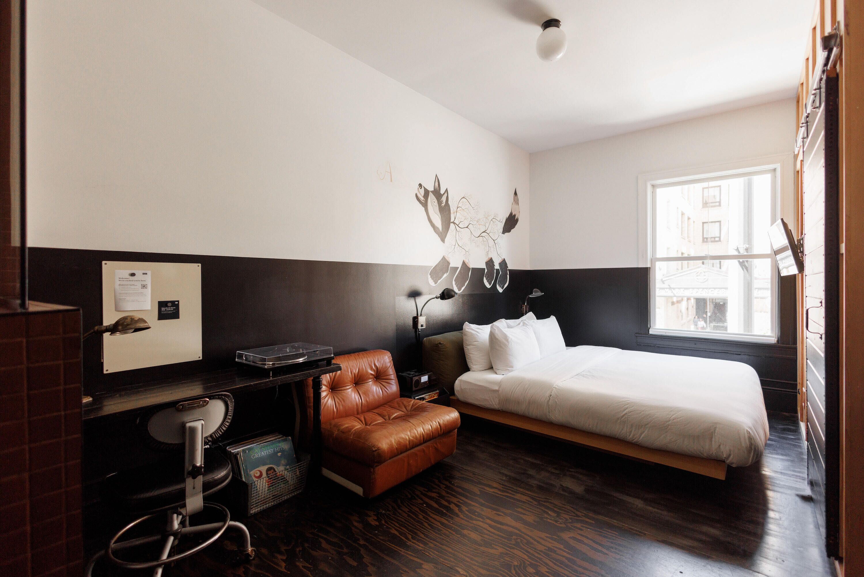 Une chambre à coucher comprenant un lit, un fauteuil en cuir marron, un bureau avec un ordinateur et une lampe fixée au mur.