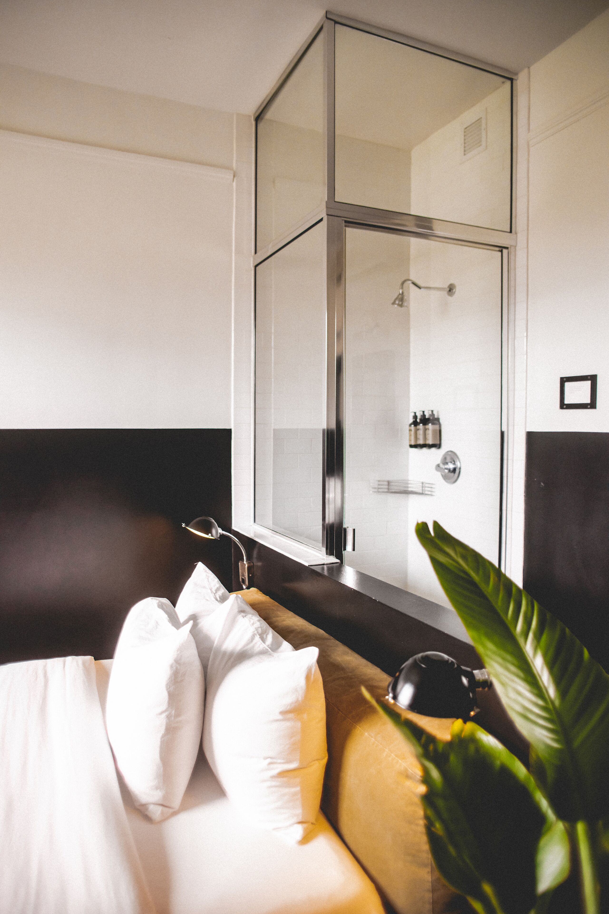 A modern hotel room with a bed, a glass-enclosed shower, and a bedside table with toiletries.