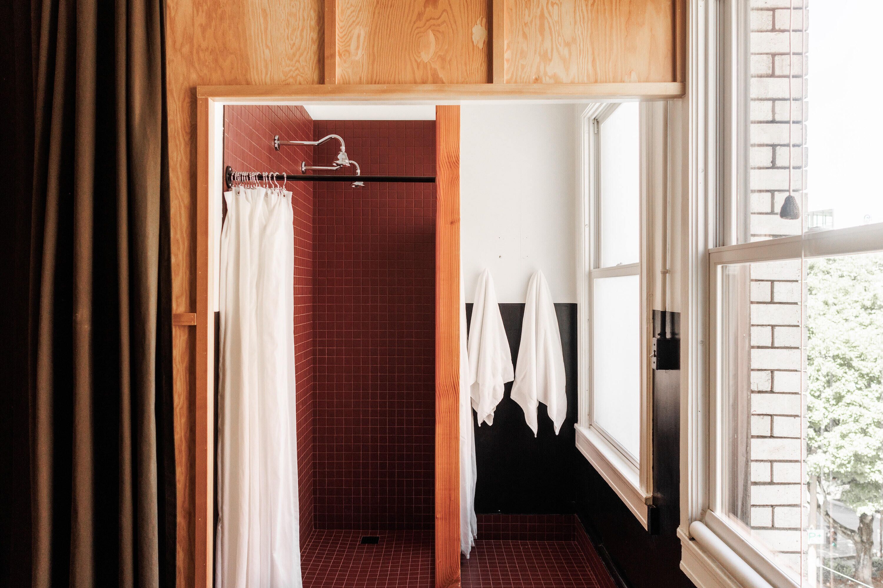 Un baño con ducha de azulejos rojos, armarios de madera y ventana con vistas a la vegetación.