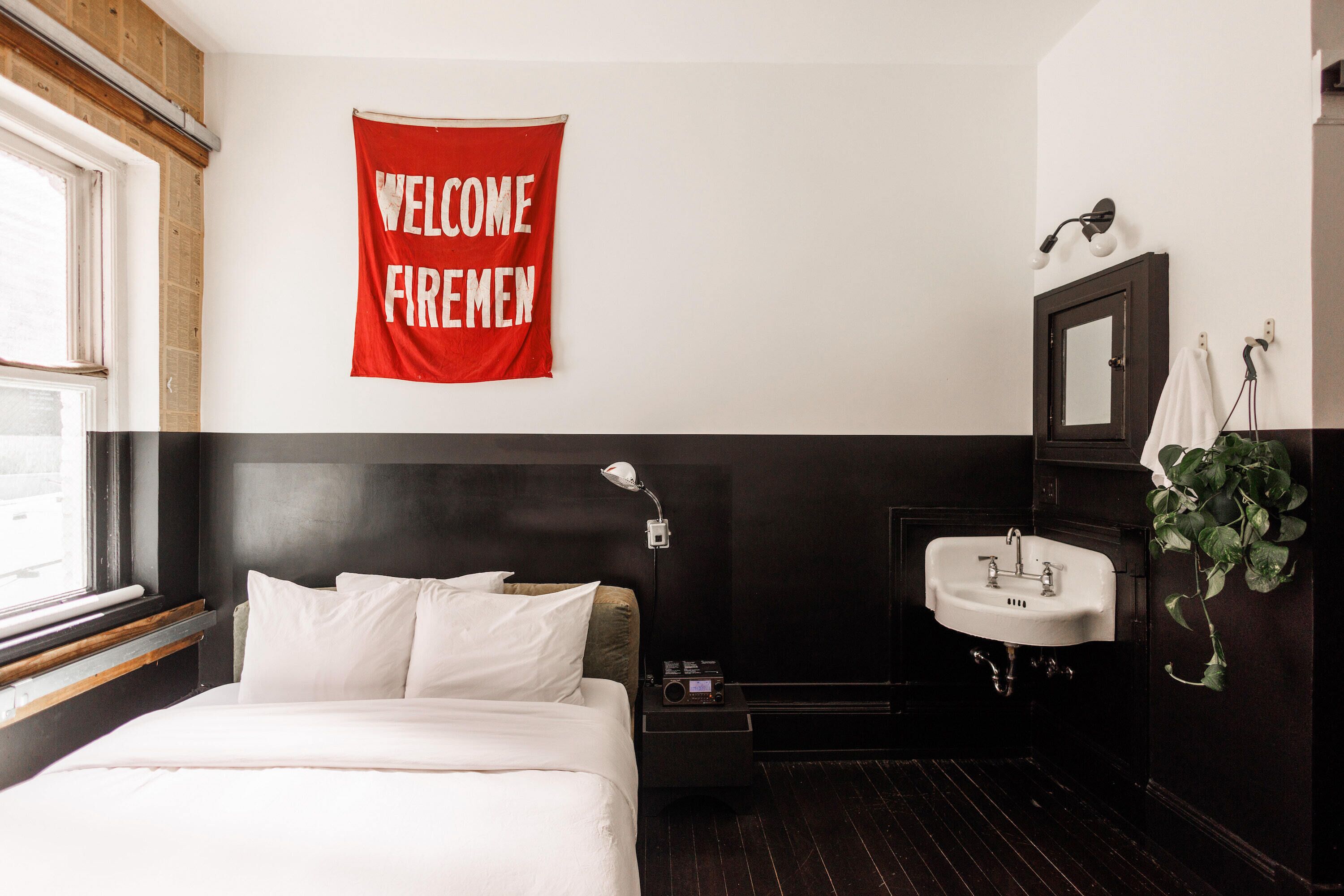 Une chambre d’hôtel avec un lit, une table de chevet, une banderole rouge de bienvenue, un lavabo et un miroir.