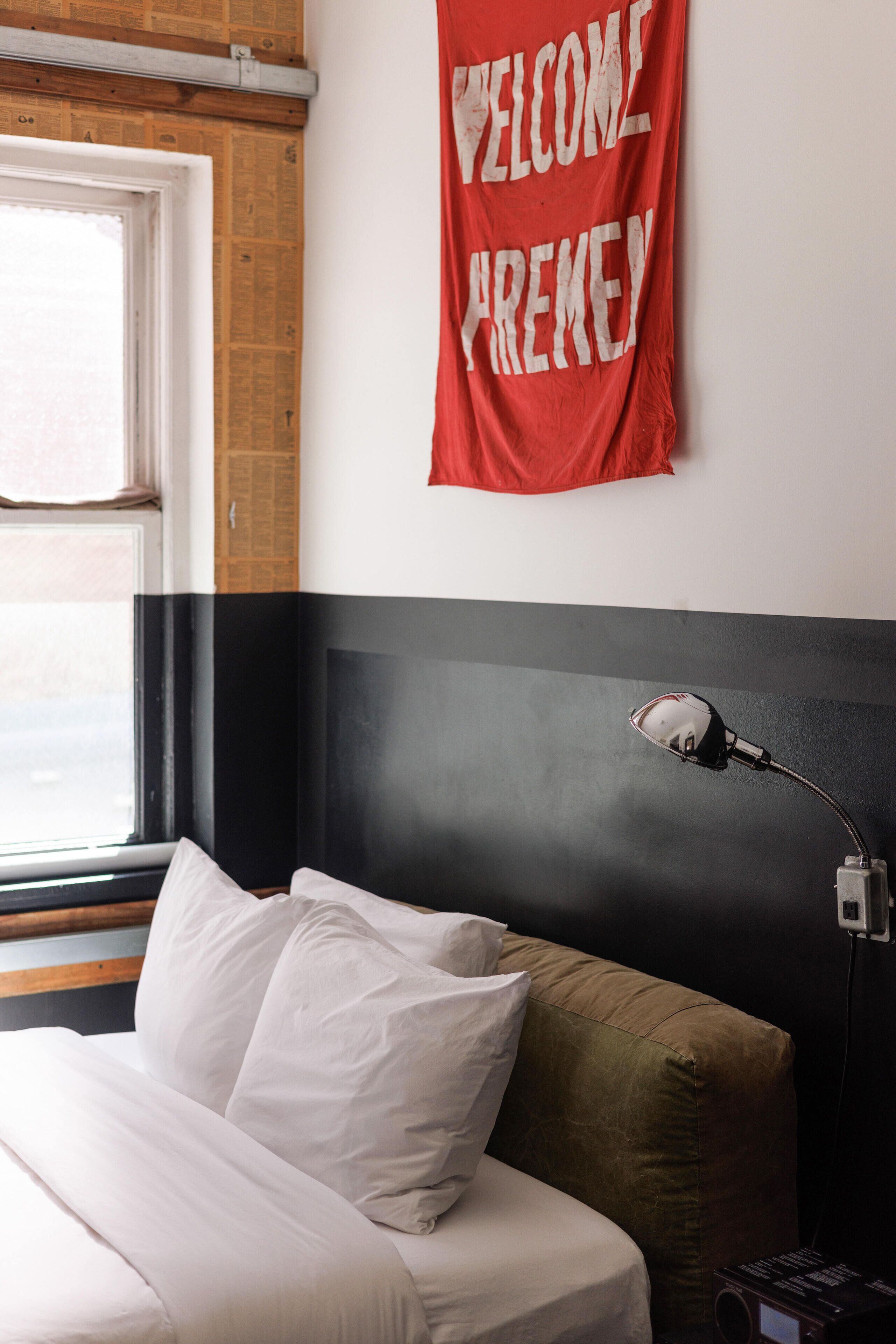 A hotel room with a bed, a red welcome sign, a lamp, and a window.