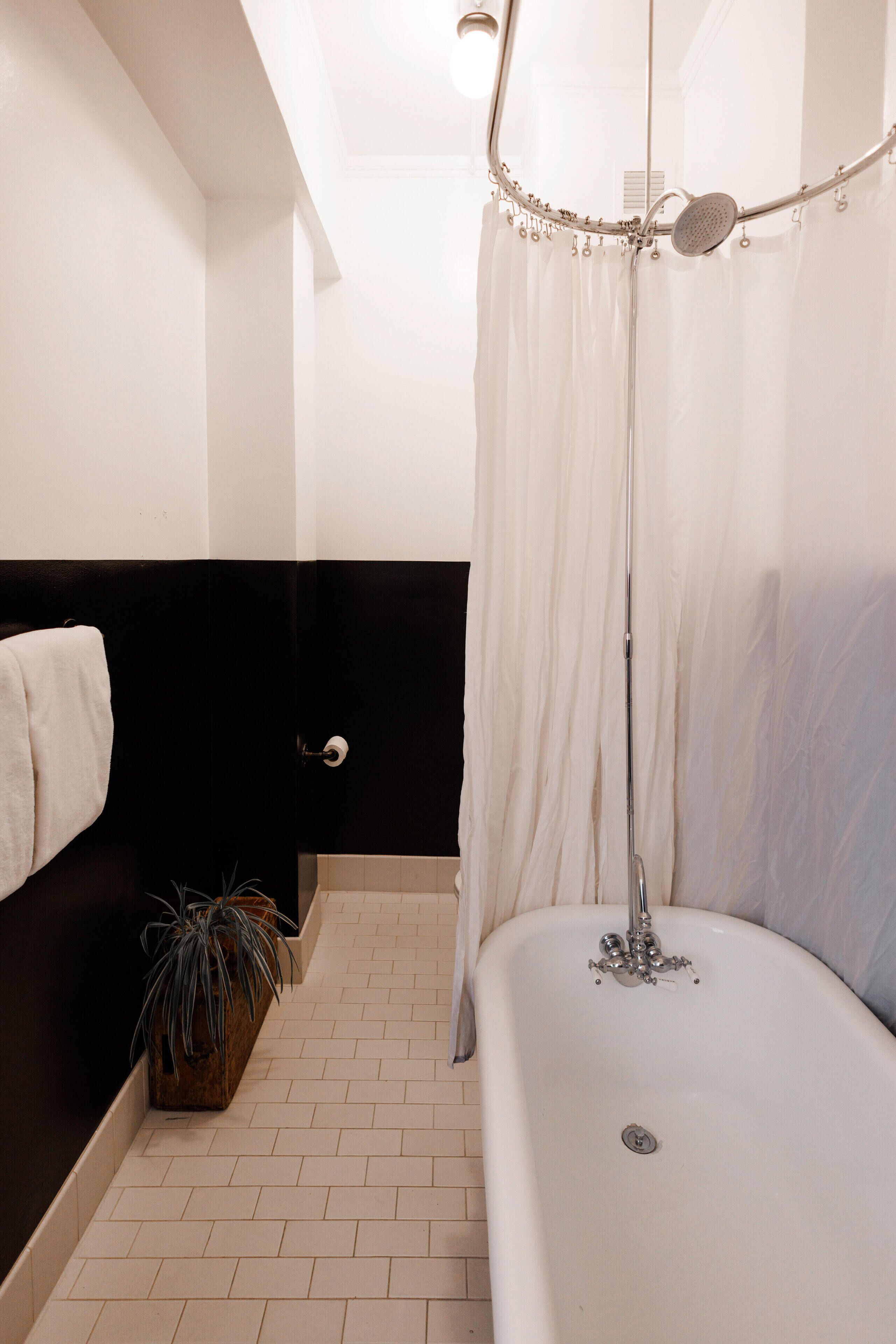 A bathroom with a bathtub, a shower with a curtain, a towel rack, and a potted plant.