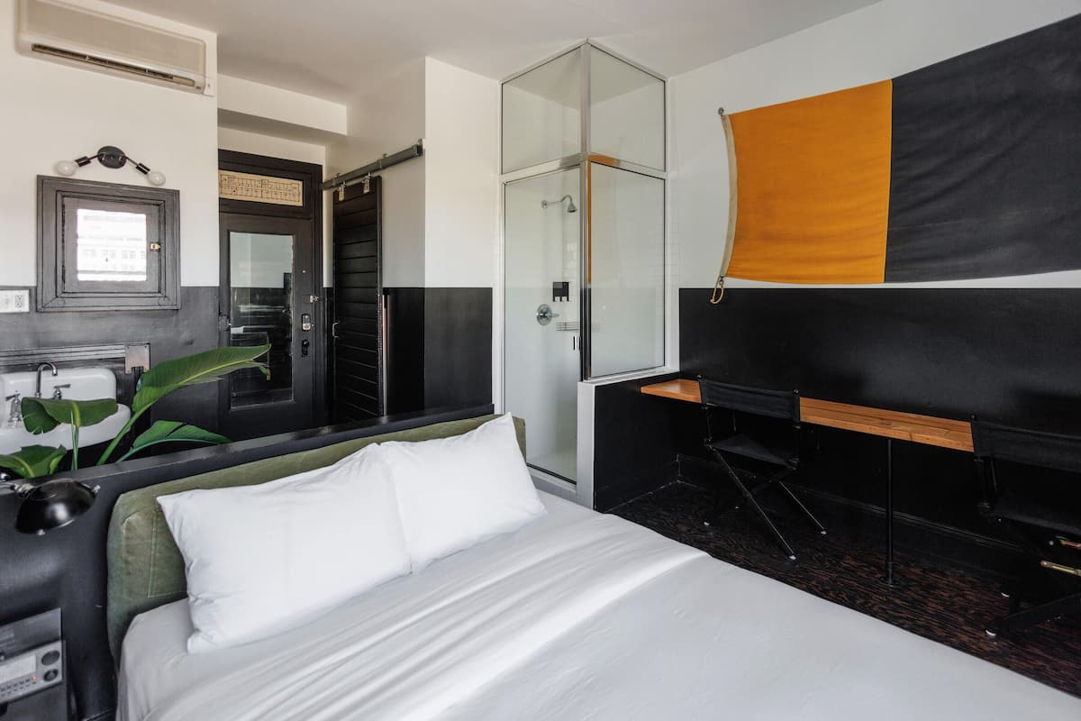 Een hotelkamer met een bed, een bureau, een douche en een groot raam.