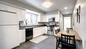 A modern kitchen with white cabinets, stainless steel appliances, and a wooden dining table. - Unique, Converted Bakery In Historic Highlands (Edmonton)