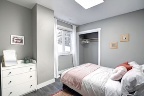 Une chambre à coucher avec un lit, une commode, une fenêtre et un placard.