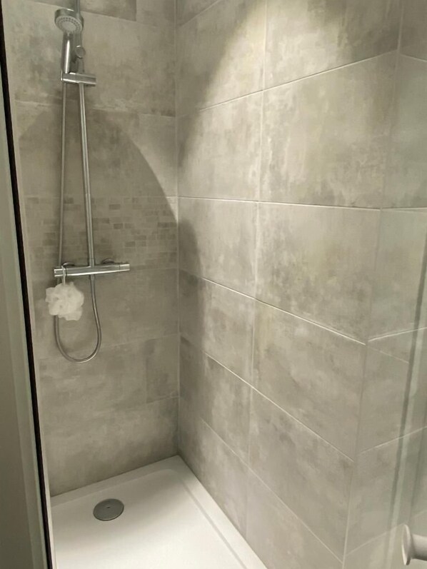 A shower with a handheld showerhead and a wall-mounted faucet.
