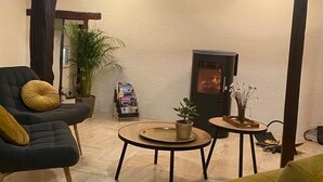 En hyggelig stue med pejs, en sort lænestol, en gul lænestol og et lille bord med en plante.