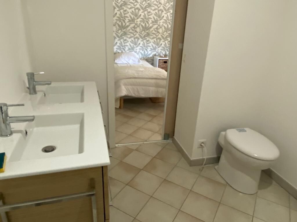 Een badkamer met twee wastafels, een toilet en een bed dat door een open deur zichtbaar is.