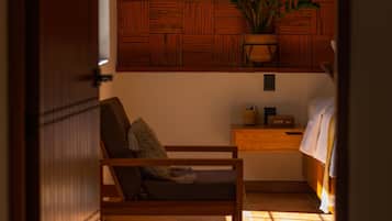 Una habitación con un panel de madera, una lámpara de mimbre, una planta, un banco de madera, una mesita de noche y una cama.