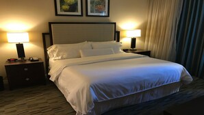 Una habitación de hotel con una cama grande, dos mesitas de noche con lámparas, un reloj y cuadros en la pared.
