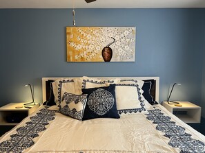Un dormitorio con una cama, dos mesitas de noche, un velador, un cuadro en la pared y un ventilador de techo.