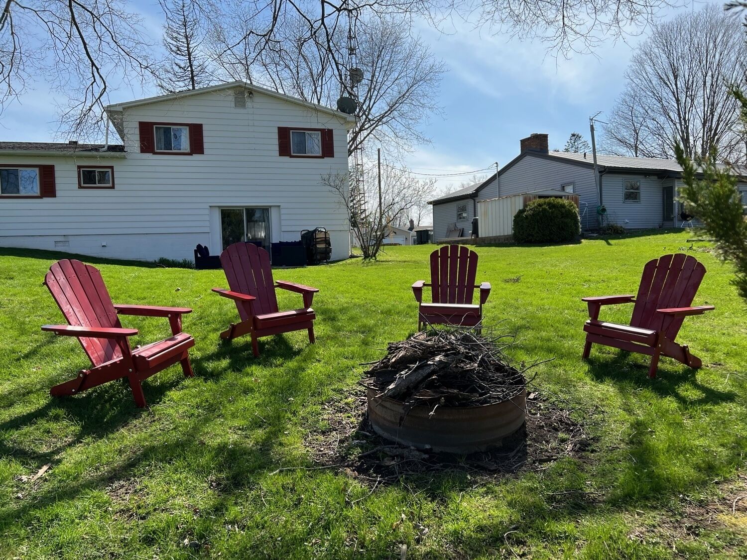 A grassy yard with four red Adirondack chairs arranged around a fire pit.