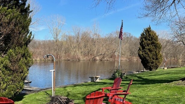 Un entorno junto al lago con sillas Adirondack rojas, un brasero y una bandera estadounidense.