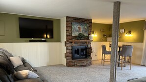 Una sala de estar con chimenea, televisor montado en la pared y comedor con sillas y mesa.