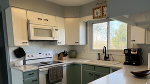 Una cocina moderna con electrodomésticos blancos, armarios verdes, un ventanal grande y una cafetera.