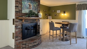 Una sala acogedora con chimenea de ladrillo, un cuadro sobre ella, y un comedor con dos sillas y una mesa.