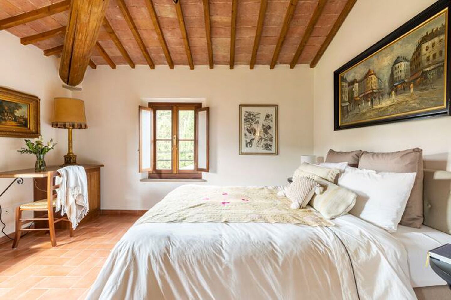 Een slaapkamer met een groot bed, een bureau met lamp, een raam en een schilderij aan de muur.