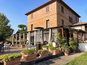 A brick building with a covered outdoor seating area and potted plants.
