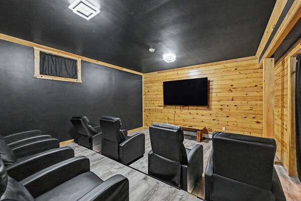 Un salón de conferencias con un televisor de pantalla plana grande montado en la pared, sillas de cuero negro dispuestas alrededor de una mesa de vidrio y paneles de madera en las paredes.