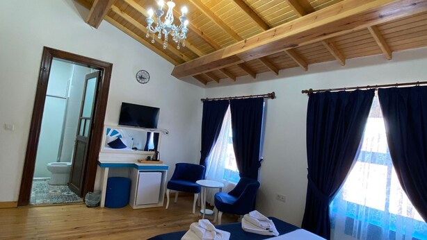 A hotel room with a wooden ceiling, a bed, a desk with a chair, and a TV.