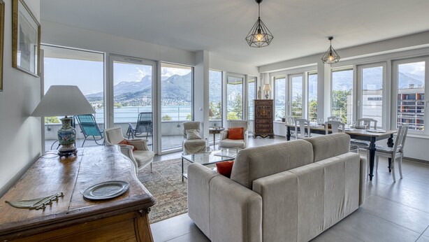 A spacious living area with a sofa, dining table, and chairs, large windows with a mountain view, and a decorative vase on a wooden table. - La Cantonade 4* - Breathtaking view of Lake Annecy (Annecy)