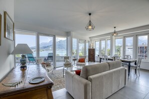 Un vaste espace de vie comprenant un canapé, une table à manger et des chaises, de grandes fenêtres offrant une vue sur les montagnes, et un vase décoratif posé sur une table en bois.