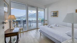 A bedroom with a bed, a desk, a chair, and a view of a mountain through large windows. - La Cantonade 4* - Breathtaking view of Lake Annecy (Annecy)