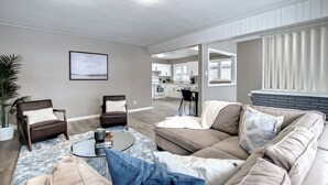 Ett modernt vardagsrum med en soffa, fåtöljer och ett soffbord. I bakgrunden syns ett kök.
