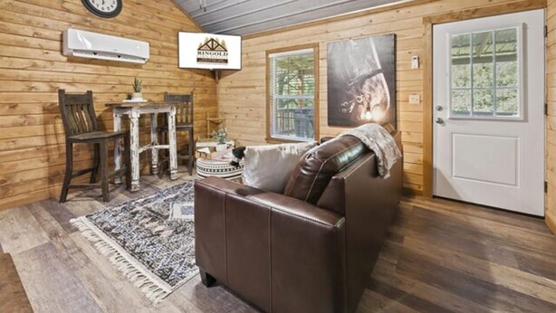 Une pièce chaleureuse avec un canapé en cuir marron, une table à manger en bois entourée de chaises, une horloge et un tableau encadré accroché au mur.