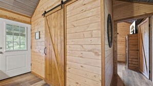 Un intérieur en bois avec une grande porte coulissante de style grange, une porte blanche avec une fenêtre et une fenêtre circulaire sur le mur.