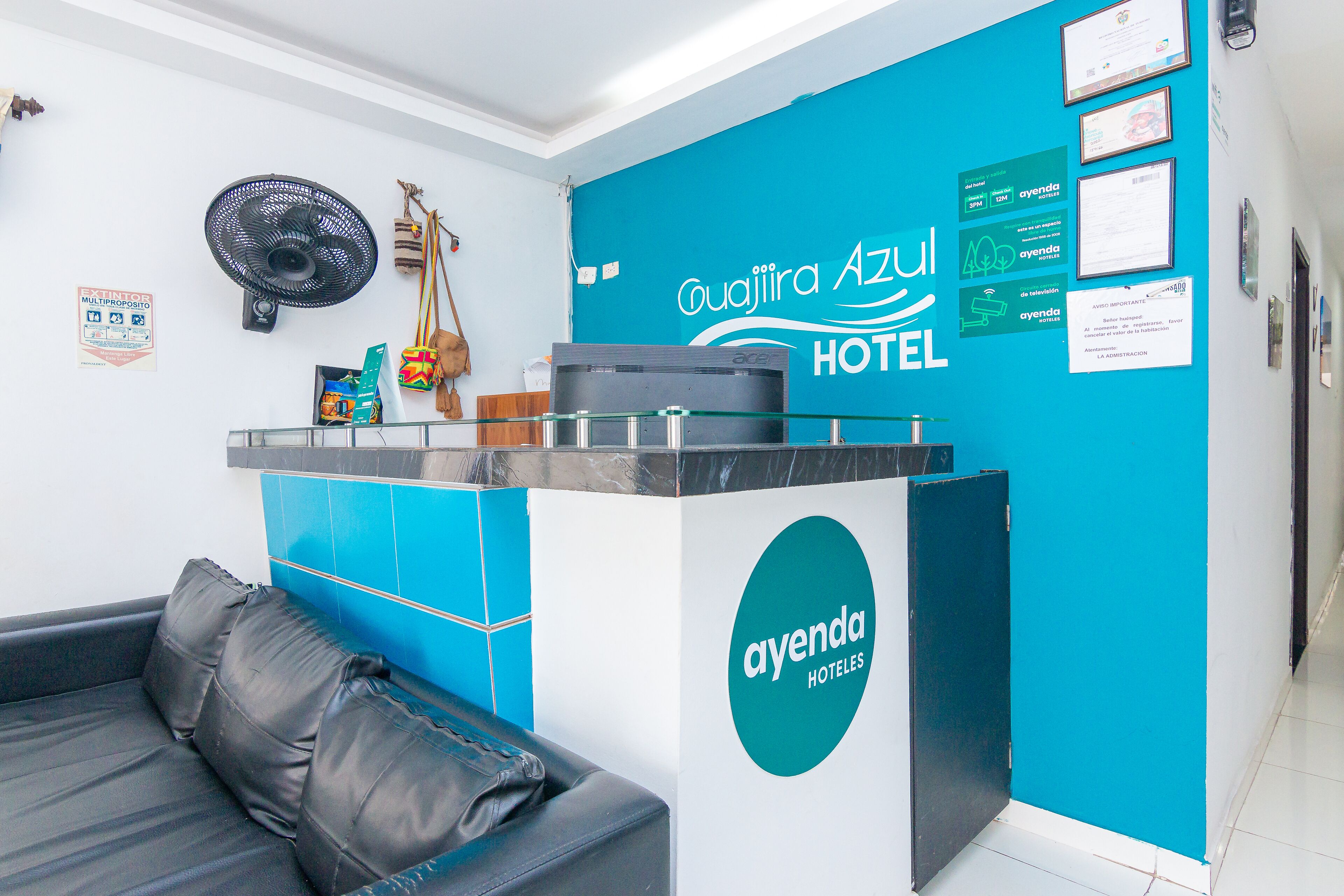 A hotel reception area with a blue and white color scheme, a black leather sofa, and a fan on the wall.