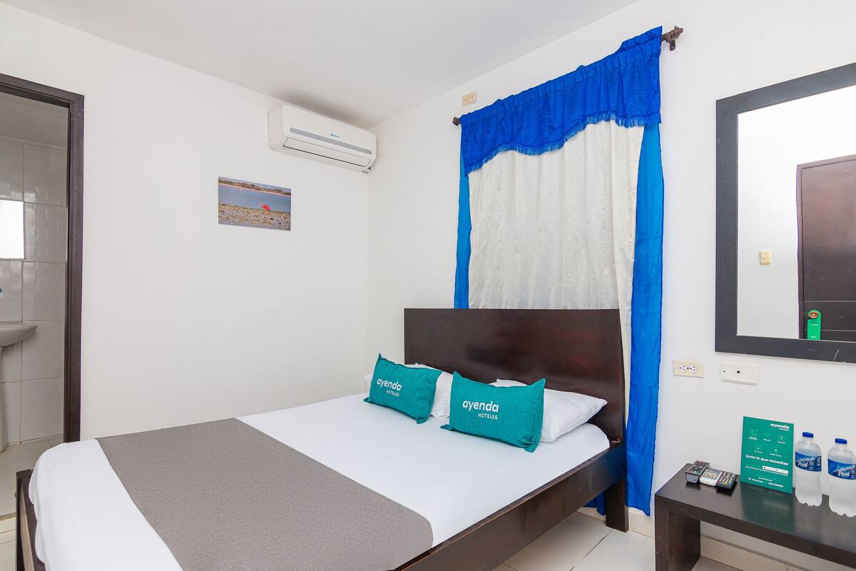 Une chambre d’hôtel avec un lit, une table de chevet avec une télécommande et un climatiseur fixé au mur.