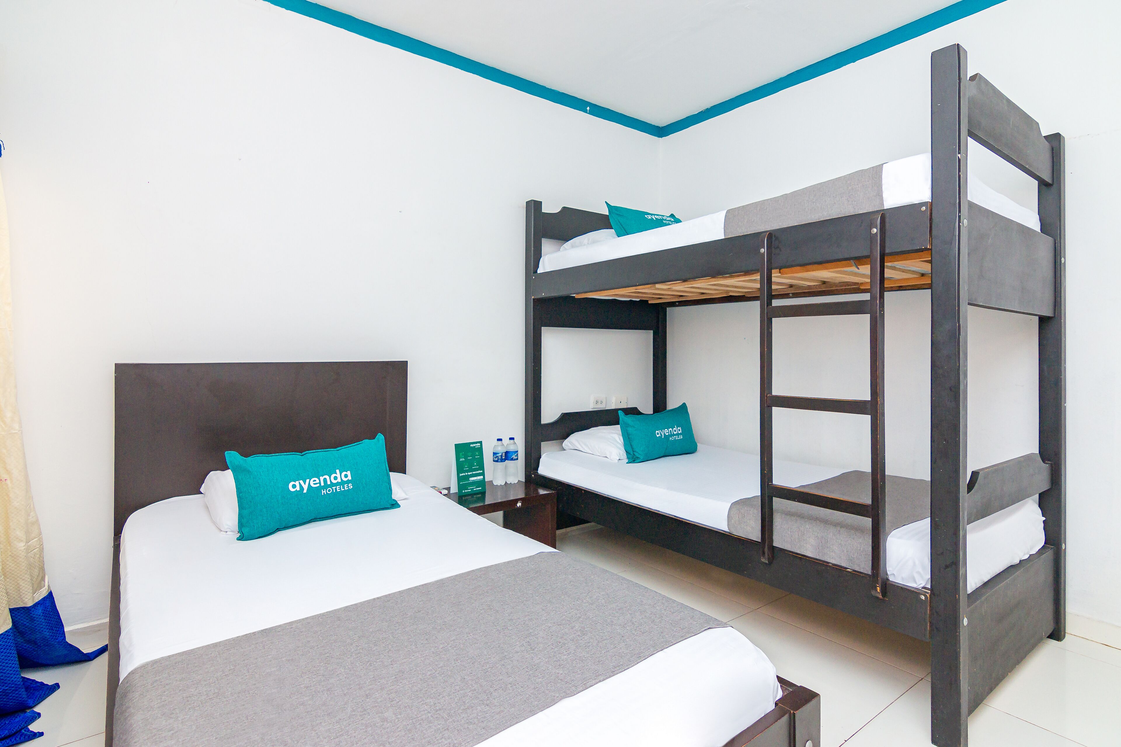 A hotel room with a bunk bed, a single bed, and a nightstand with a water bottle and a sign.