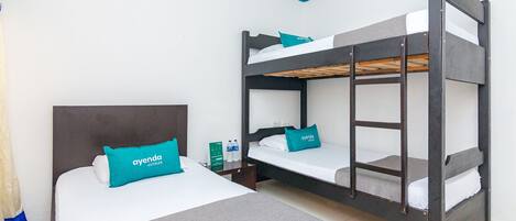 A hotel room with a bunk bed, a single bed, and a nightstand with a water bottle and a sign.