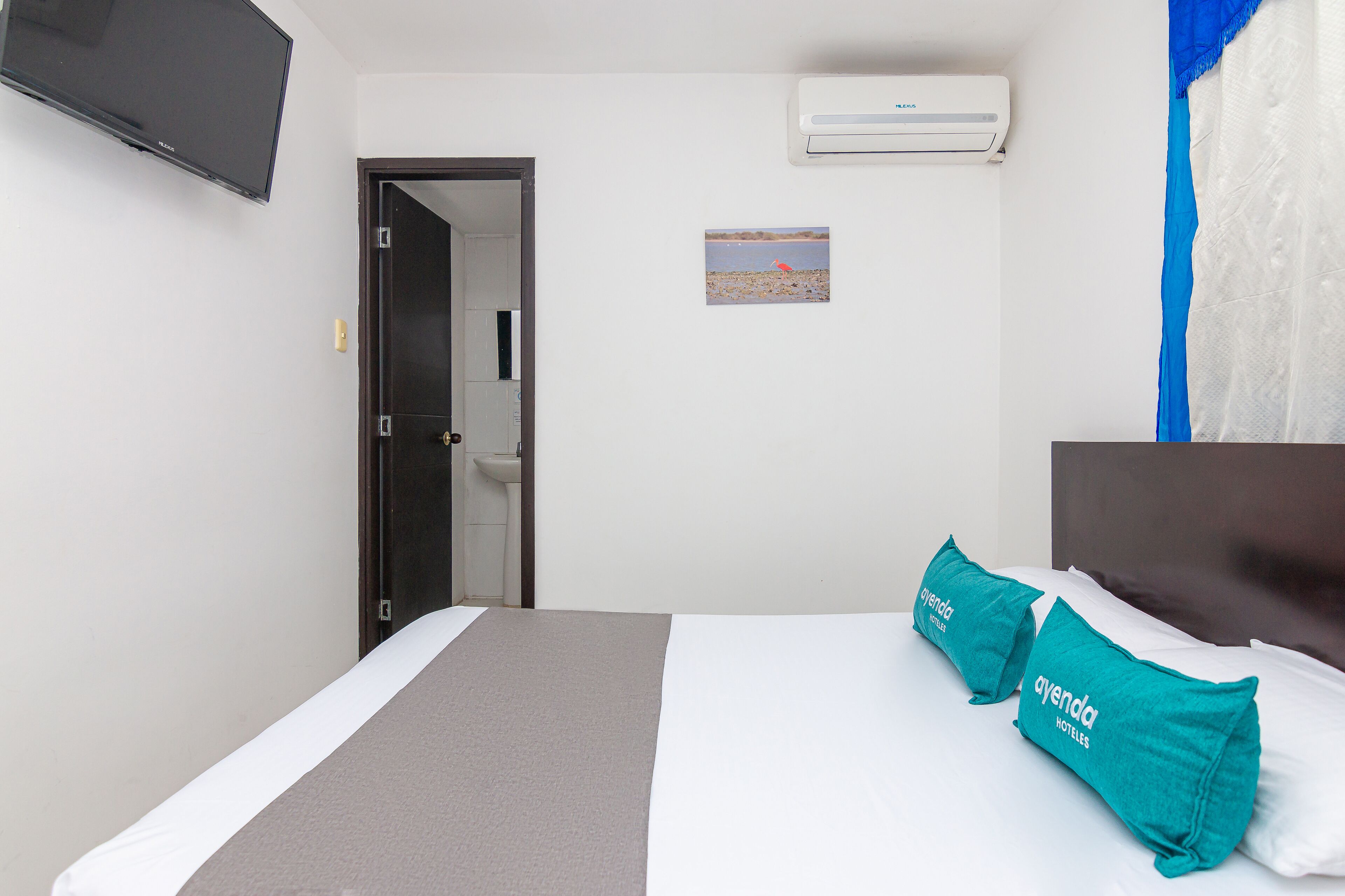 Quarto de hotel com cama, televisão de tela plana, ar condicionado e porta para o banheiro.