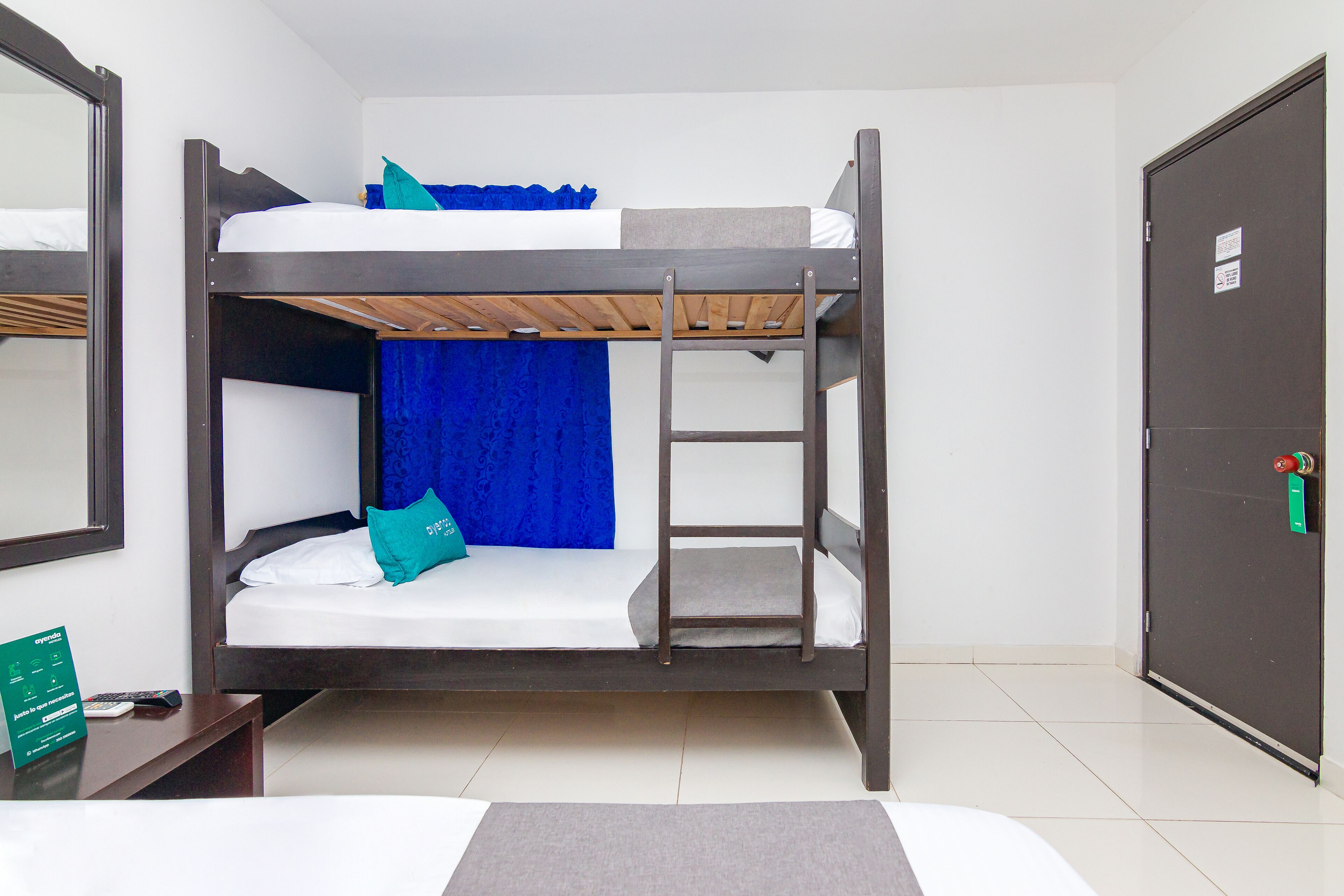 Un letto a castello con una scala, una tenda blu e un tavolino con un telecomando.