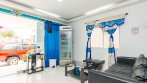 A reception area with a sofa, a glass table, a refrigerator, and a blue curtain. - Hotel Guajira Azul (Riohacha)