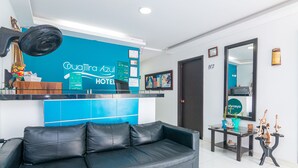 A hotel reception area with a blue wall, a black leather sofa, a reception desk, and a mirror. - Hotel Guajira Azul (Riohacha)