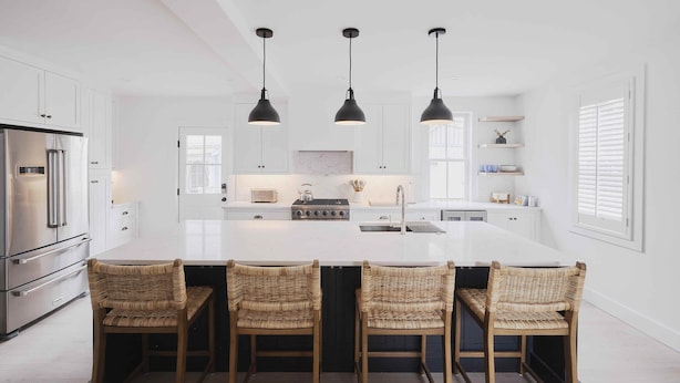 Una cocina moderna con armarios blancos, una isla central con taburetes y luminarias colgantes.